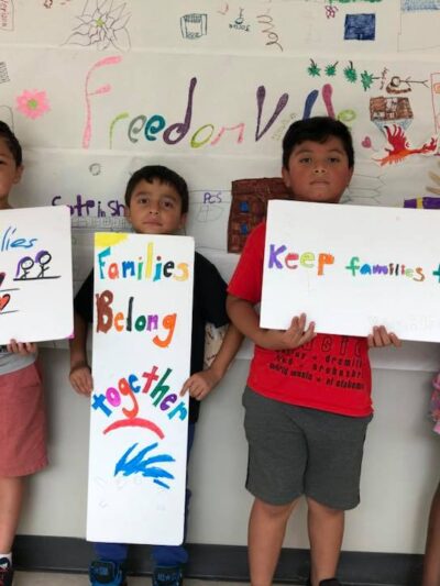 Three students from the Somerville Freedom School hold handmade signs: Keep Families Together