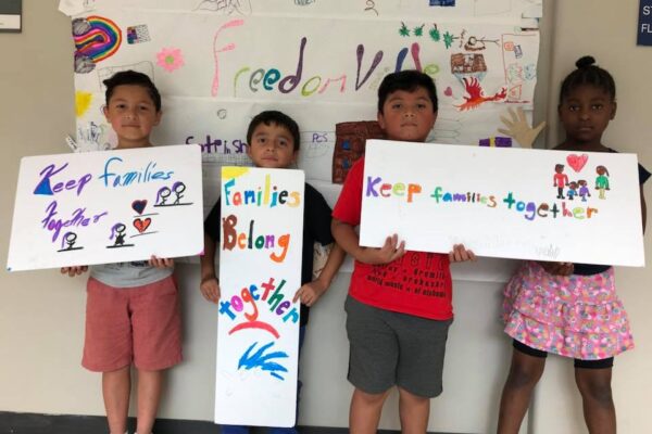 Three students from the Somerville Freedom School hold handmade signs: Keep Families Together