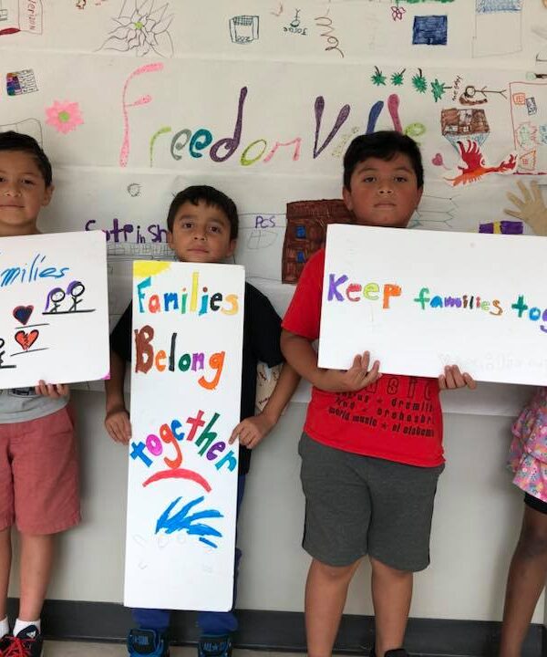 Three students from the Somerville Freedom School hold handmade signs: Keep Families Together