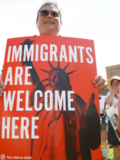 person holding 'immigrants are welcome here' sign at rally