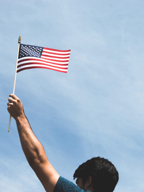 person holds american flag in front of blue sky