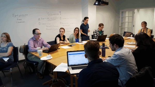 Phone bankers sit at table listening to Olivia Santoro, volunteer coordinator, explain how to phone bank