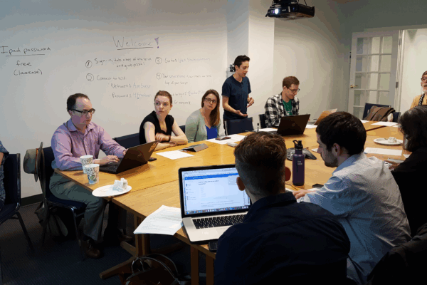 Phone bankers sit at table listening to Olivia Santoro, volunteer coordinator, explain how to phone bank