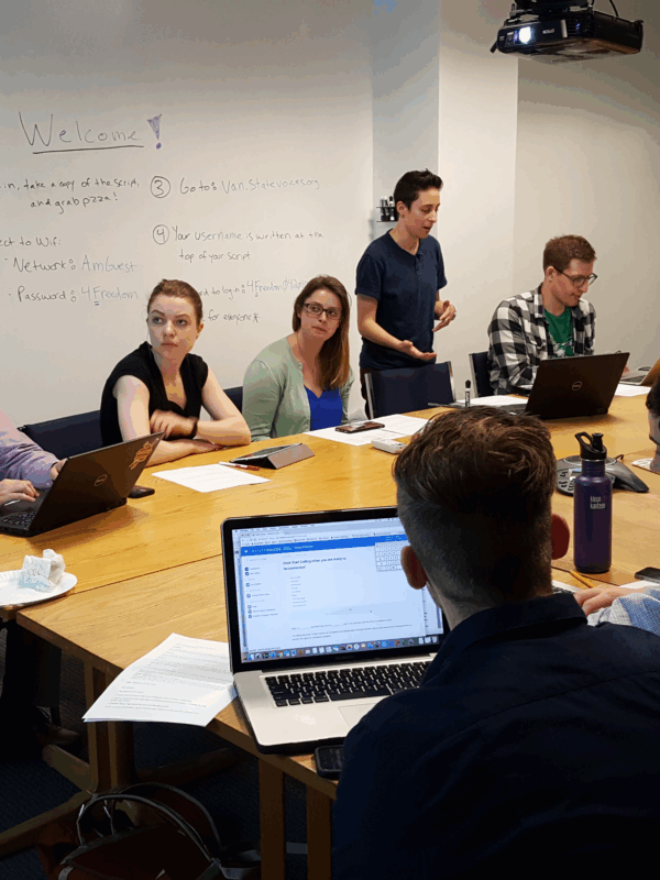 Phone bankers sit at table listening to Olivia Santoro, volunteer coordinator, explain how to phone bank