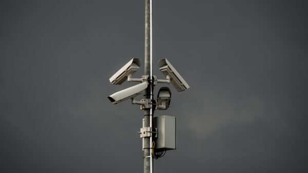 Three surveillance cameras mounted on a poll in front of gray sky