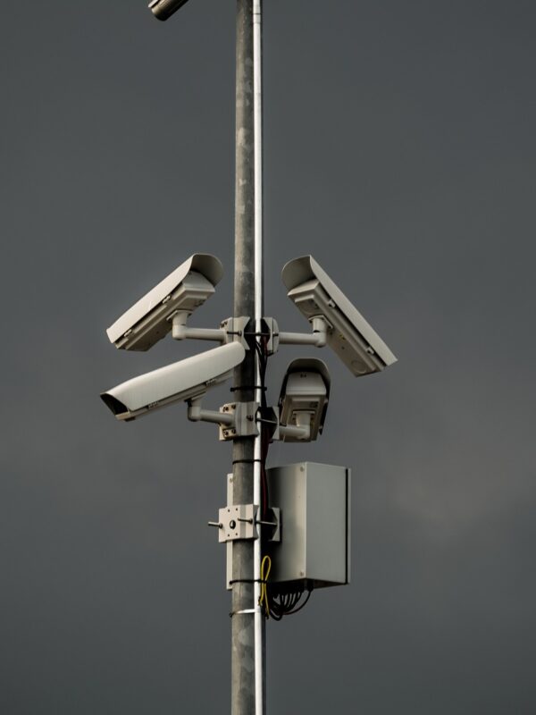 Three surveillance cameras mounted on a poll in front of gray sky