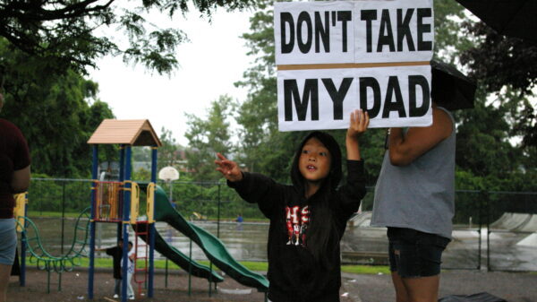 A child holds a sign saying "Don't take my Dad," after a raid on immigrants in Lowell, Mass.