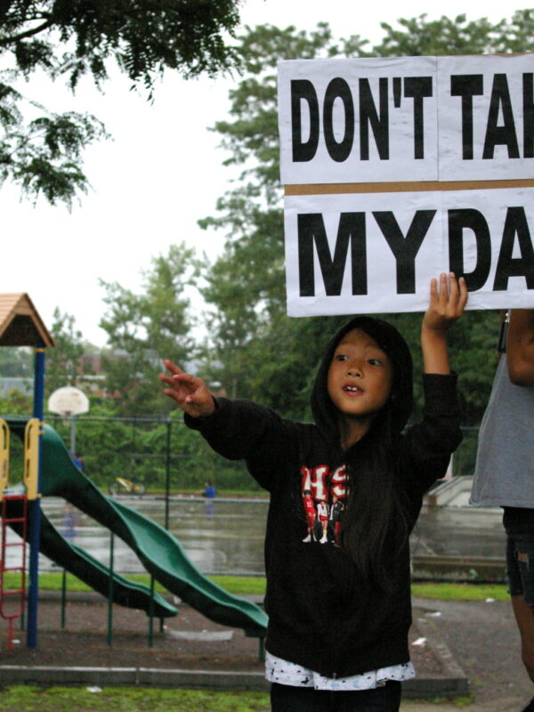 A child holds a sign saying "Don't take my Dad," after a raid on immigrants in Lowell, Mass.