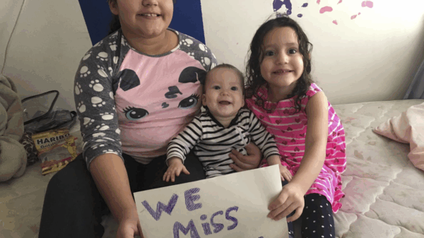 Pereira Brito's three children sit on a bed with a handwritten "We miss you" sign