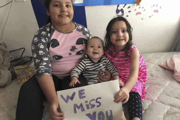 Pereira Brito's three children sit on a bed with a handwritten "We miss you" sign