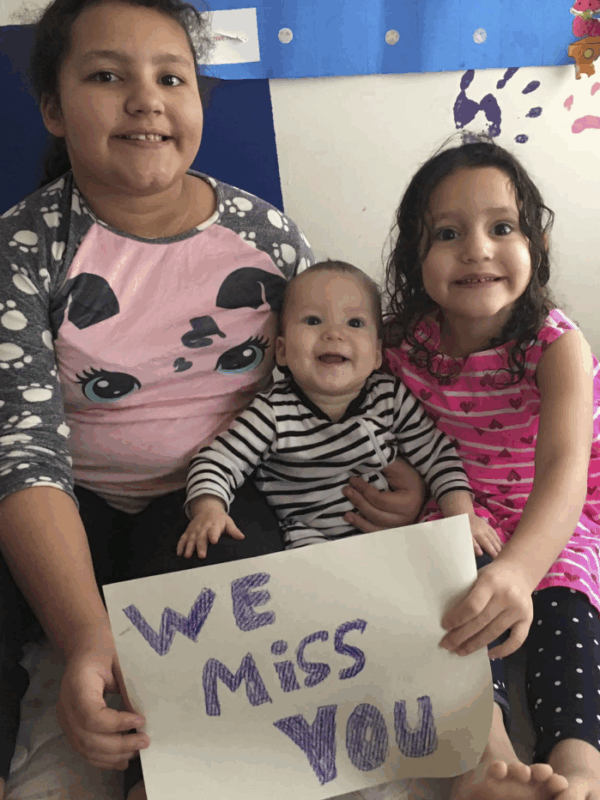 Pereira Brito's three children sit on a bed with a handwritten "We miss you" sign