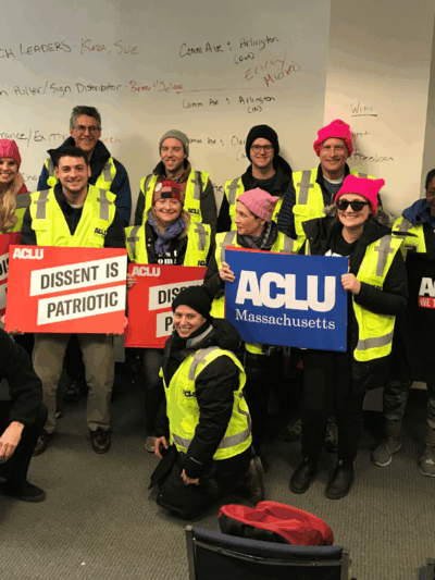 Volunteers in bright yellow ACLU vests hold ACLU signs