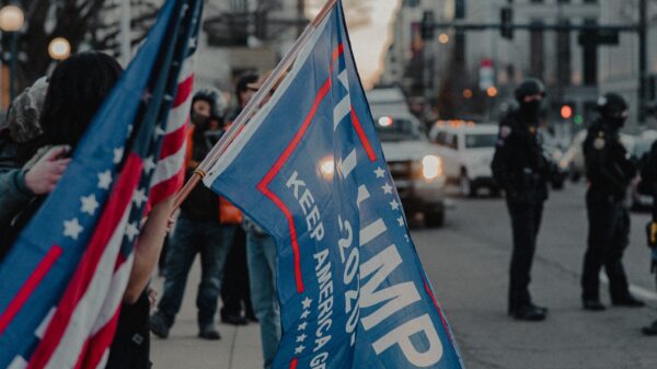 Image of TRUMP 2020 flag and American flag with city in background