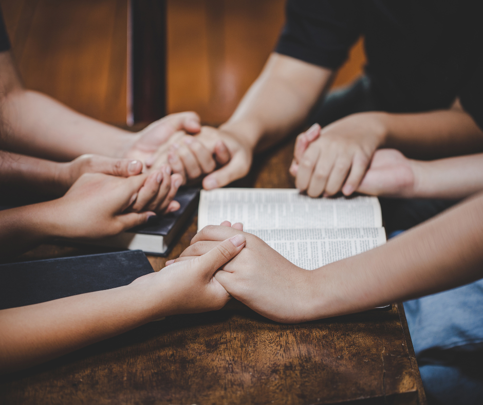 four people in a circle are holding hands over a religious text.