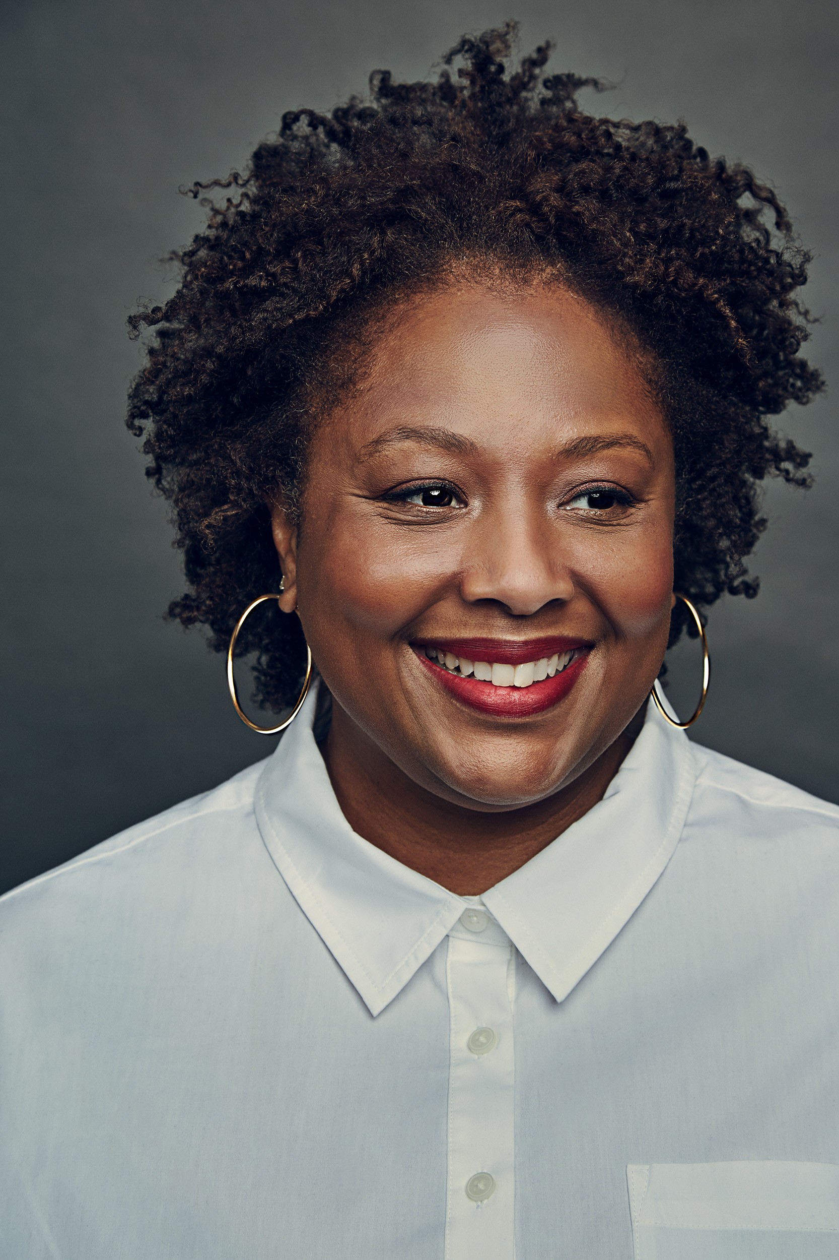 Deborah Archer is posing for a headshot, smiling, and wearing a white shirt with Gold Hoop Earrings.