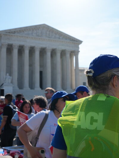 Supreme Court of the United States with rally happening outside. A crowd of people is stood outside the court.
