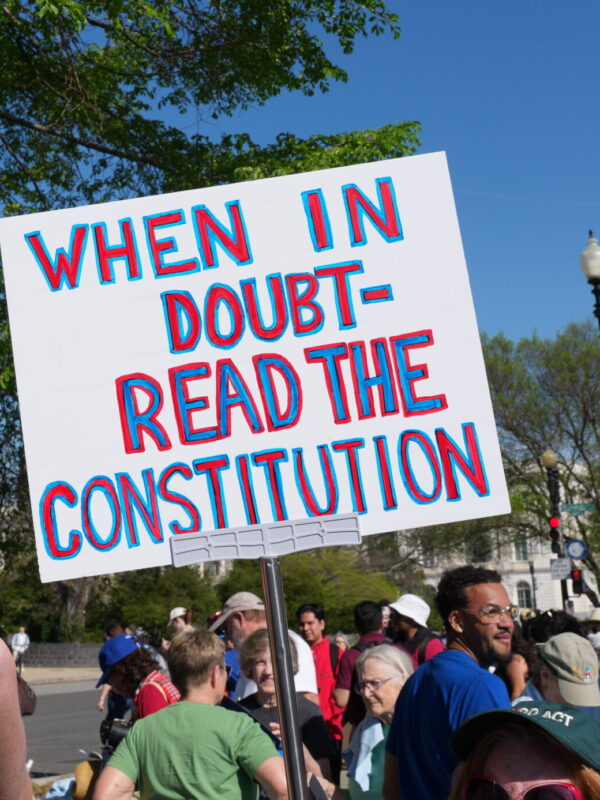 Protest sign held on the street outside the Supreme Court of the United States. The sign has a white background and reads "When in doubt-read the constitution" in red letter with a blue outline.