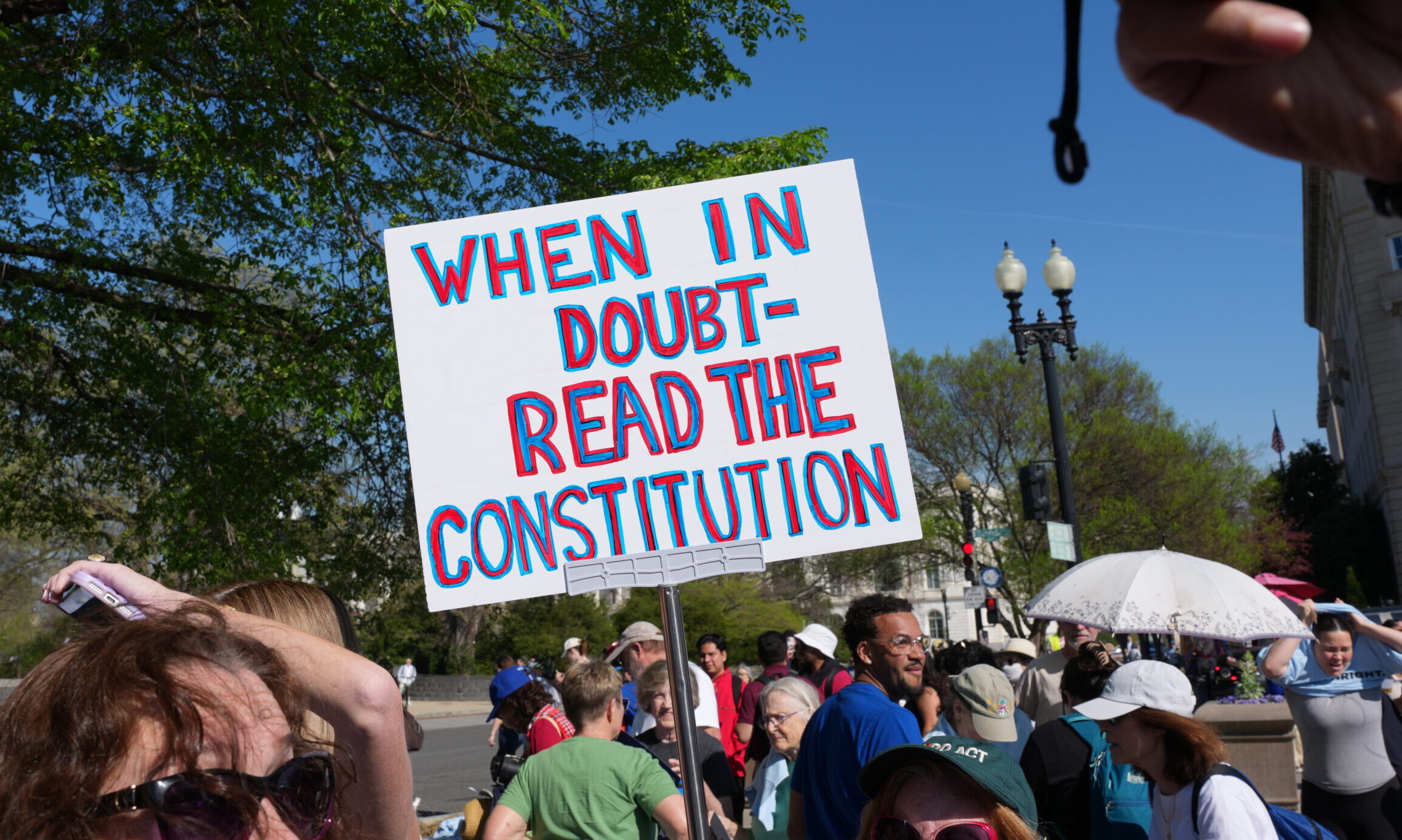 Protest sign held on the street outside the Supreme Court of the United States. The sign has a white background and reads "When in doubt-read the constitution" in red letter with a blue outline.