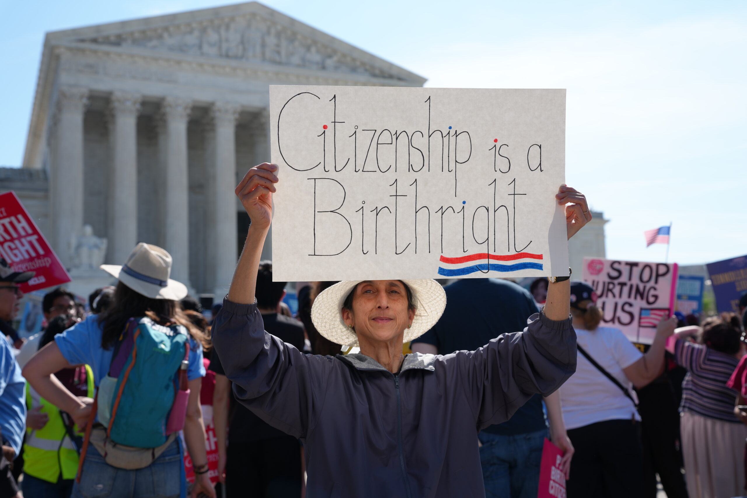 Person is seen holding a white protest sign outside the Supreme Court of the United States. The sign reads "Citizenship is a Birthright" with a red and blue underline.