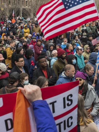 Crowd of people gathered with protest signs outside city hall plaza in Boston, MA