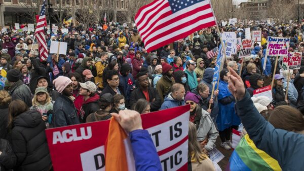 Crowd of people gathered with protest signs outside city hall plaza in Boston, MA