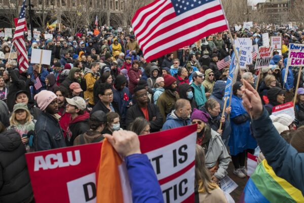Crowd of people gathered with protest signs outside city hall plaza in Boston, MA