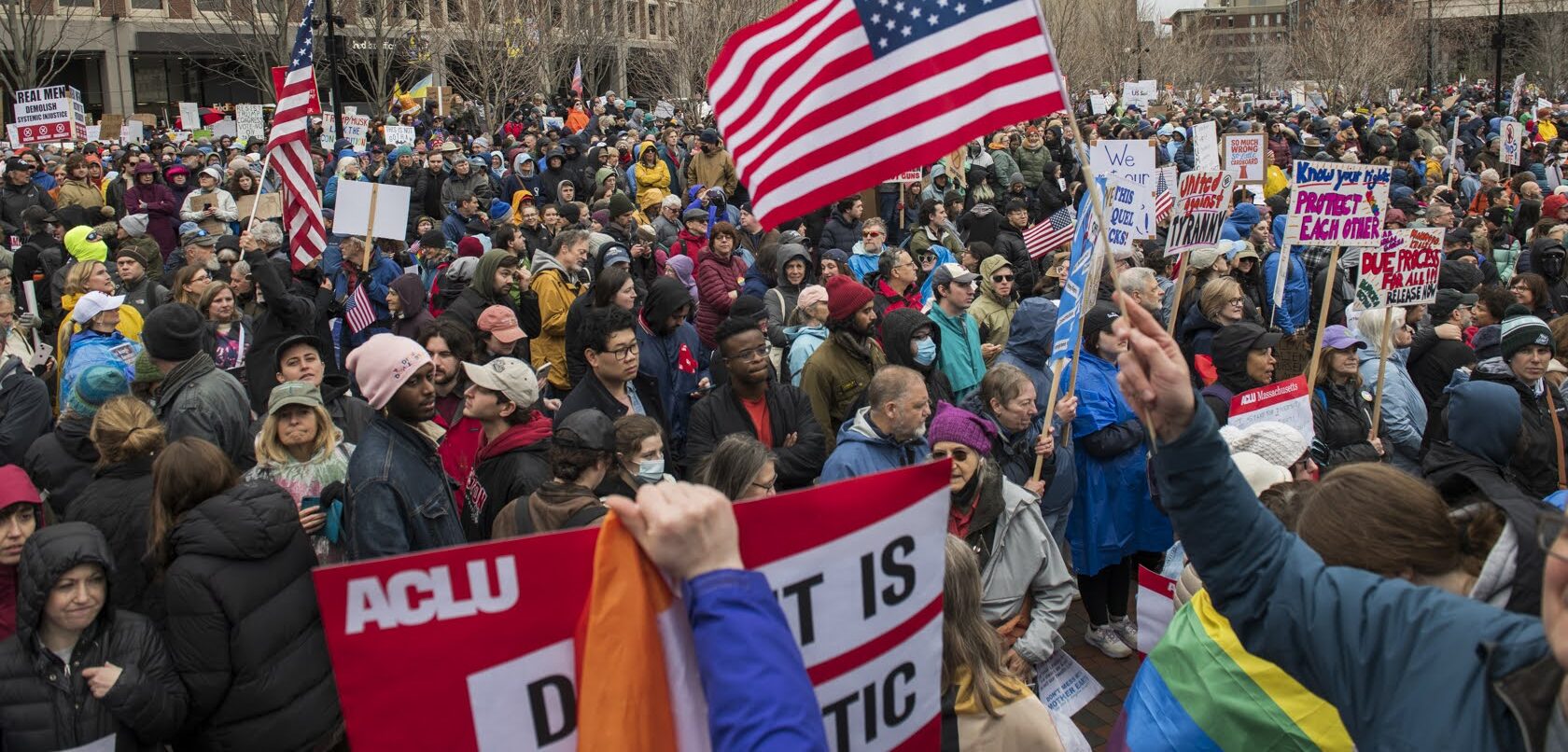 Crowd of people gathered with protest signs outside city hall plaza in Boston, MA