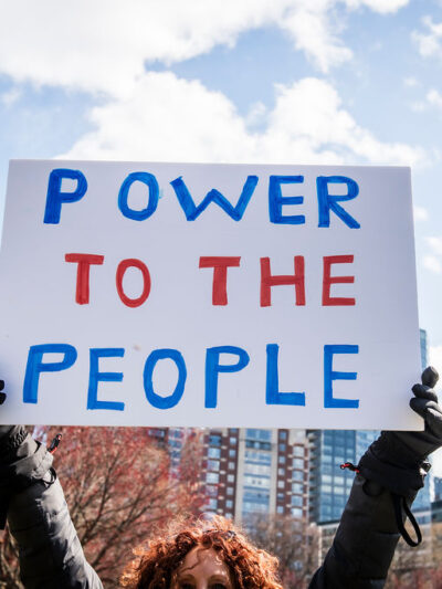 A protest sign is held in the air reading "Power to the People"