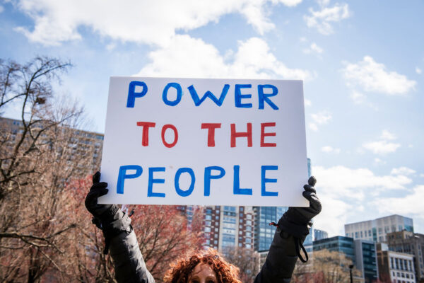 A protest sign is held in the air reading "Power to the People"
