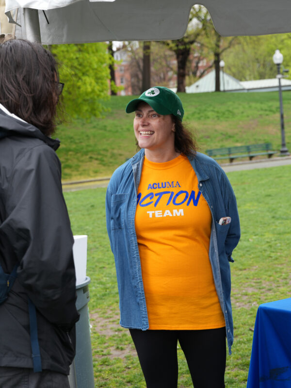 ACLU Volunteer is seen speaking to a member of the public at an event. She is wearing a yellow shirt and a denim button up.