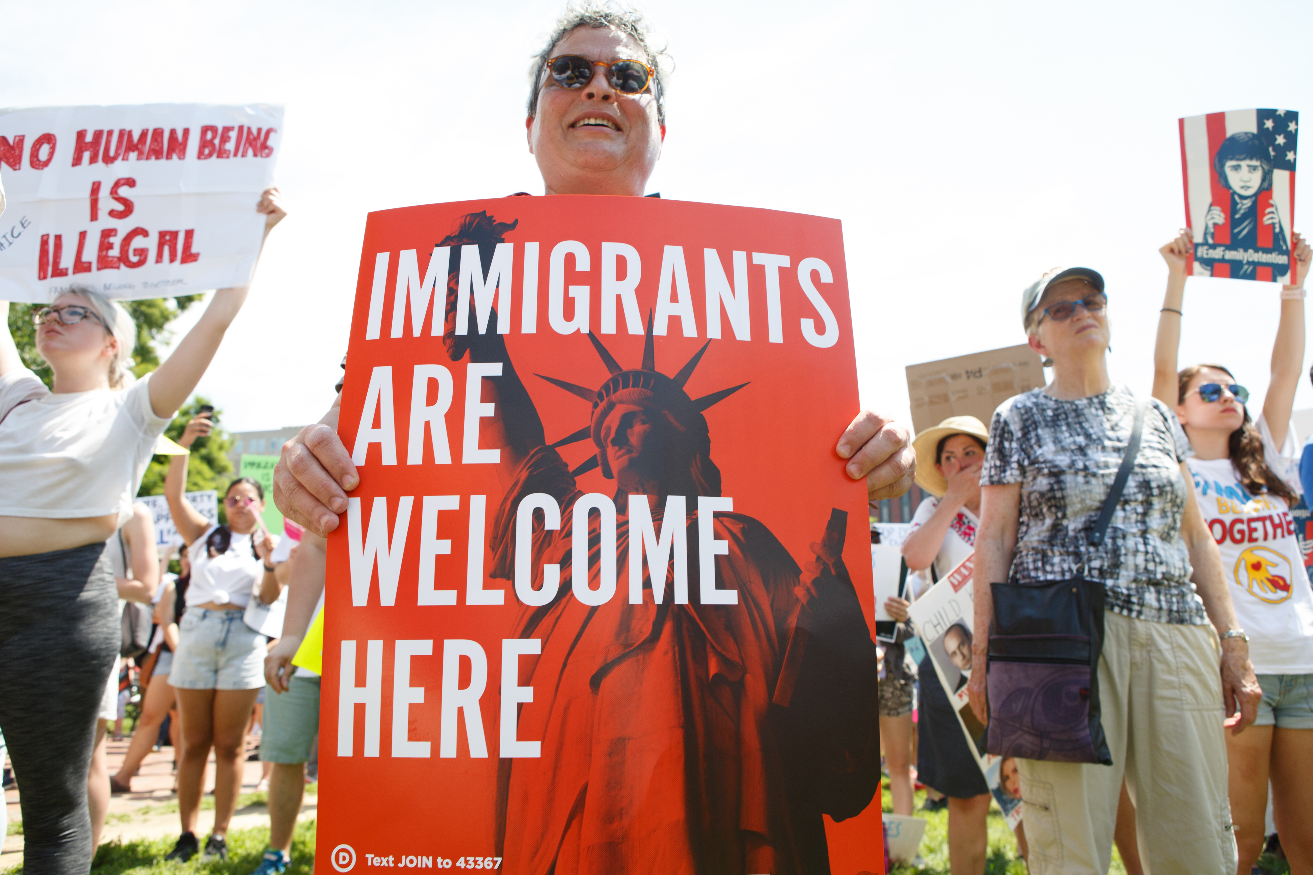 person holding 'immigrants are welcome here' sign at rally