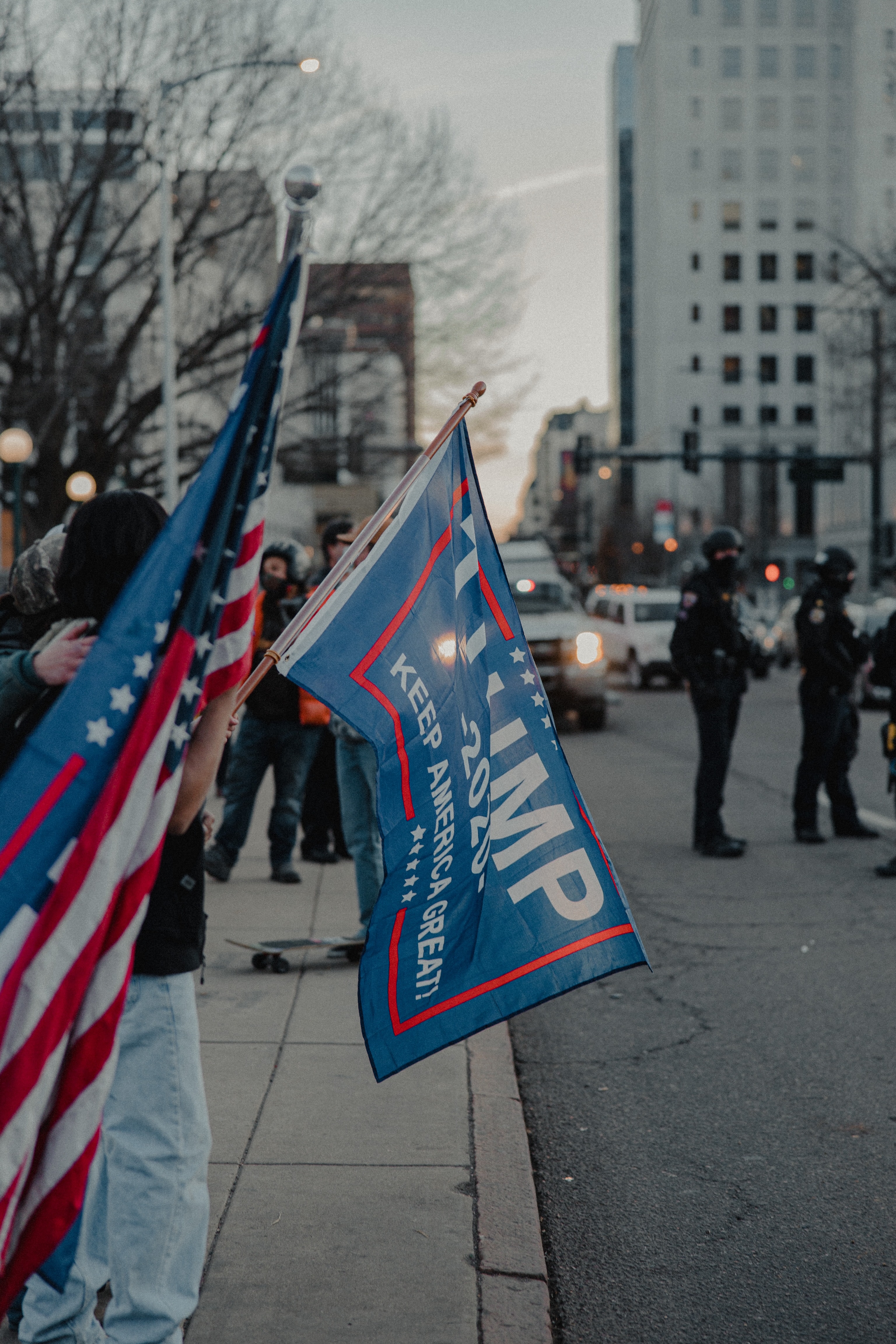 Image of TRUMP 2020 flag and American flag with city in background