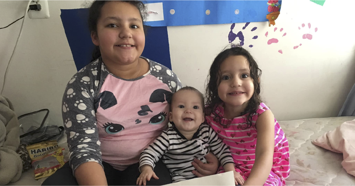 Pereira Brito's three children sit on a bed with a handwritten "We miss you" sign