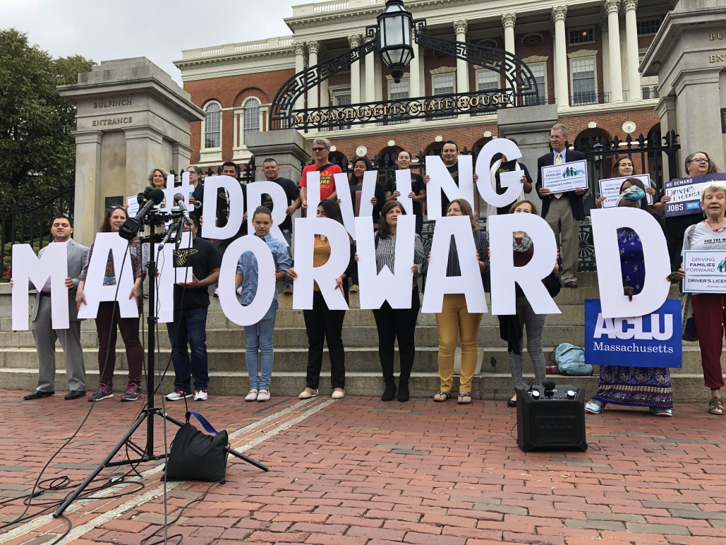 Supporters hold letters spelling "Driving MA Forward" on State House steps