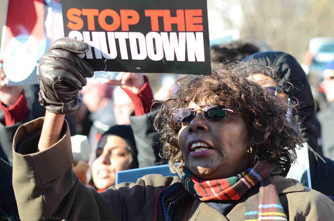 Protestor stands with "stop the shutdown" sign