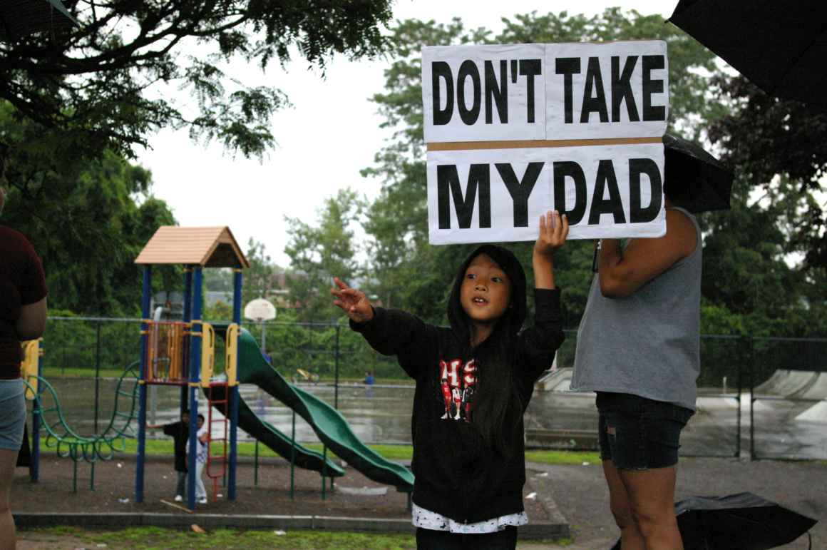 A child holds a sign saying "Don't take my Dad," after a raid on immigrants in Lowell, Mass.