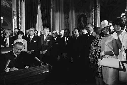 President Lyndon B. Johnson signs the Voting Rights Act of 1965 on August 6 while Martin Luther King and others look on.