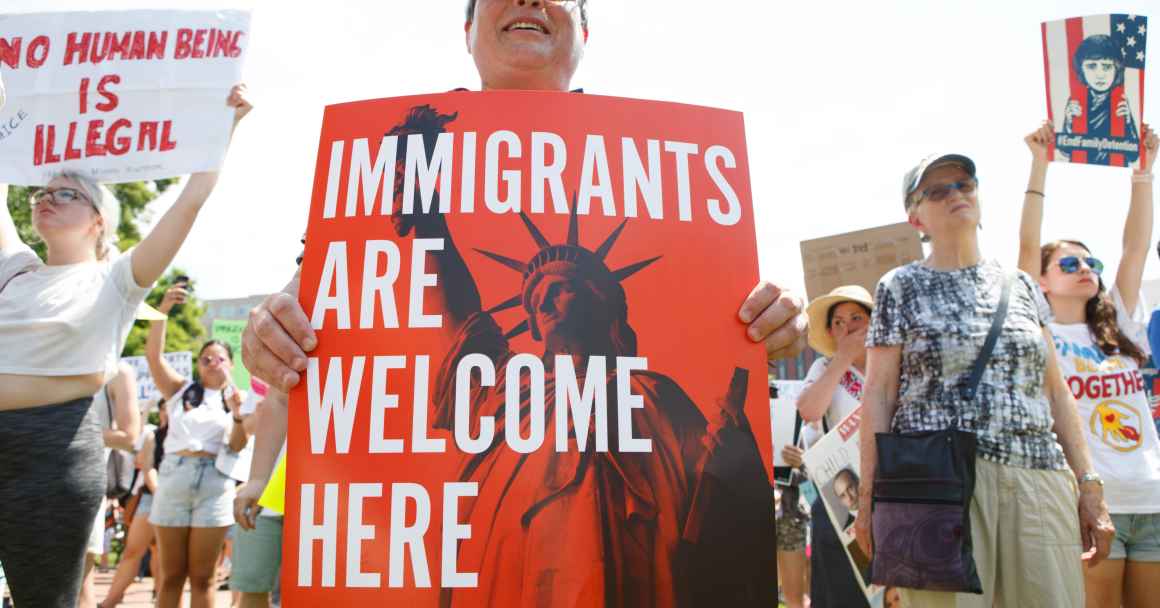 person holding 'immigrants are welcome here' sign at rally