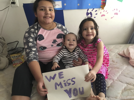 Pereira Brito's three children sit on a bed with a handwritten "We miss you" sign