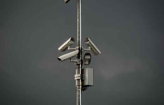 Three surveillance cameras mounted on a poll in front of gray sky