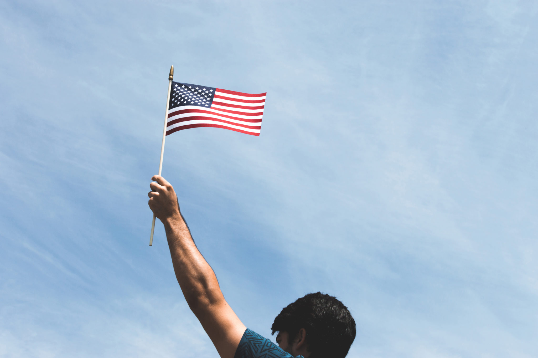 person holds american flag in front of blue sky